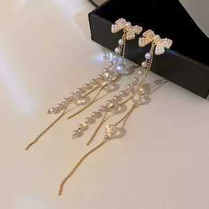 Détail des boucles d'oreilles nœud en perles avec longues pampilles dorées et cristaux