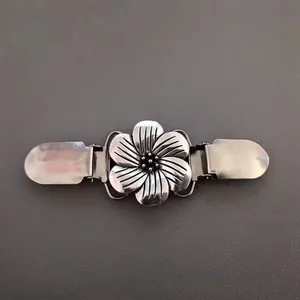 Gros plan sur un clip à pull vintage en forme de fleur argentée avec détails ciselés