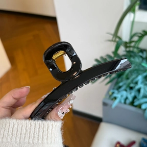 Close-up of a large black glossy hair claw clip with strong gold metal spring mechanism