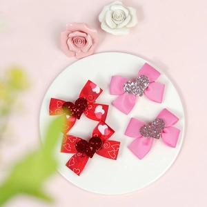 Close-up of four red and pink ribbon hair bows with glitter hearts on a white plate