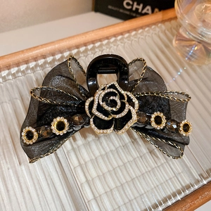 Détail d'une pince à cheveux avec nœud en maille noire, camélia en strass et perles