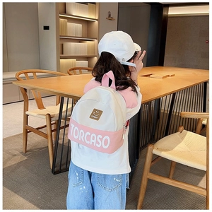 Rear view of a toddler wearing a pink and white patchwork backpack in a cozy room