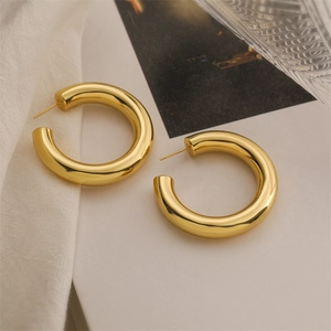 Detailed close-up of thick gold-plated hollow teardrop earrings on marble background