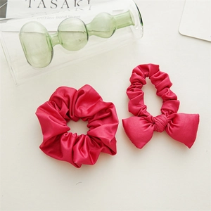 Close-up of rose red satin bow scrunchies with silky texture on white background