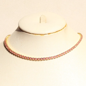 Detail of pink round-cut tennis necklace with golden base on a jewelry display stand