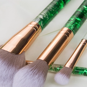 Detail of three makeup brushes with green glitter handles and rose gold ferrule detail