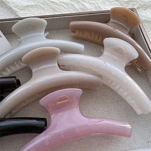 Detail shot of six curved PC shark hair clips in assorted colors on a beige tray