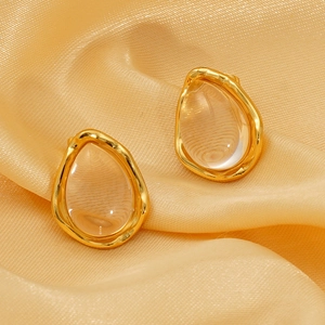 Elegant gold teardrop titanium steel earrings featuring clear resin on champagne silk fabric