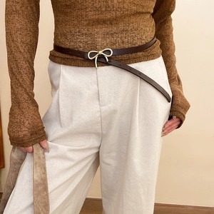 Close-up of a vintage dark brown slim leather belt featuring a golden bow metal buckle