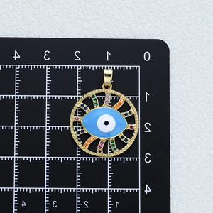 Golden evil eye pendant with blue enamel and colorful cubic zirconia on a scale mat