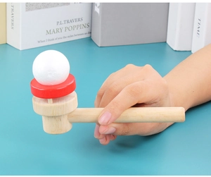 Close-up of wooden breath training toy with red tray and white foam ball in hand
