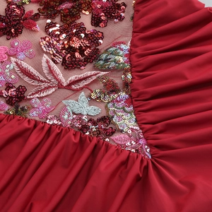 Close-up of red evening dress featuring colorful sequin floral embroidery and pleated fabric