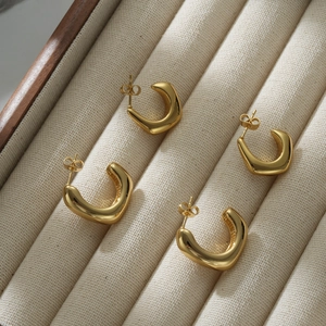 Macro shot of gold 18k C-shaped stainless steel earrings on a beige jewelry tray