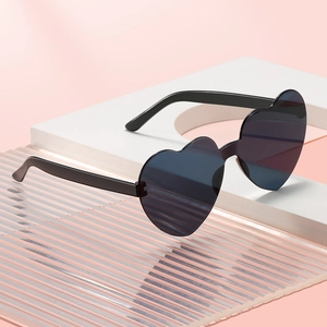 Fashionable heart-shaped rimless sunglasses with dark grey gradient lenses on a pink background