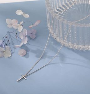 Detailed view of silver cross pendant with fine snake chain on soft blue backdrop