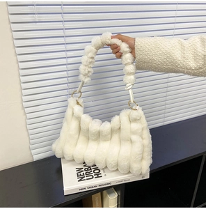 Detail of white plush handbag with striped texture, plush handle, and gold buckle on books