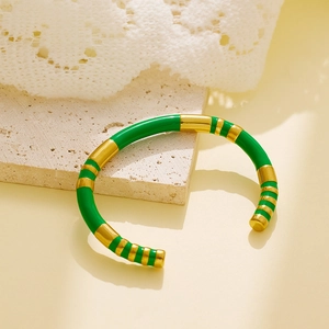 Close-up of green and gold enamel striped open bangle on a beige stone display