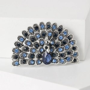 Close-up of a silver peacock brooch featuring blue rhinestones and a large crystal drop