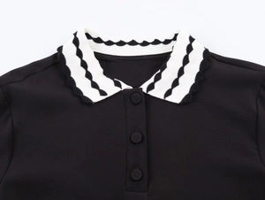 Detail of knitted women's black polo shirt with contrasting wavy pattern collar and buttons