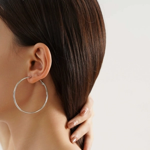 Close-up of a model wearing large silver-toned titanium steel hoop earrings