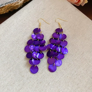 Detail shot of purple shell tassel earrings with golden hooks on beige textured fabric