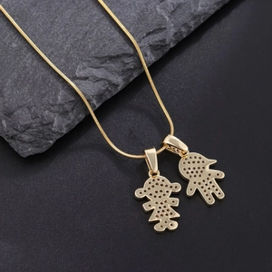 Gold plated snake chain necklace with boy and girl pendants on dark stone background