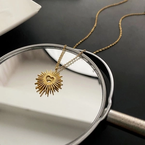 Detail of gold heart pendant with sunburst design and reflection on a black surface