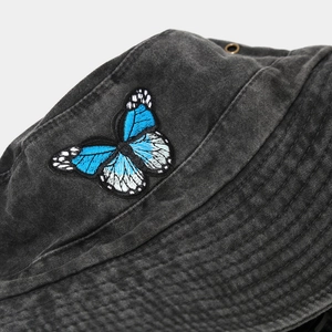 Gros plan sur la broderie papillon bleu et les œillets en métal du chapeau en jean gris