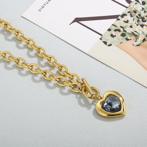 Détail du collier à grosse chaîne dorée 18k avec pendentif cœur et cristal foncé