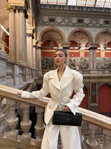 Close-up of a white structured blazer with wide lapels and a black leather handbag