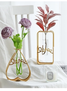 Detail of artistic gold metal love frame with glass tube vase and purple flowers