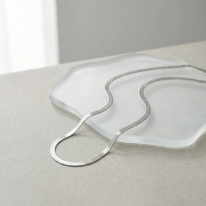 Detailed macro view of silver flat snake bone chain necklace on frosted glass tray