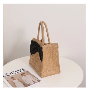 Detail of khaki straw woven handbag featuring a large black bow and braided handle