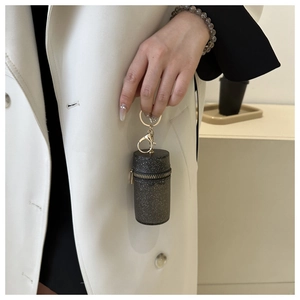 Detail of a mini cylindrical chain pouch with black glitter finish and gold metal hardware
