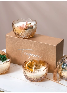 Close-up of amber glass scented candle with dried flowers and premium gold gift box