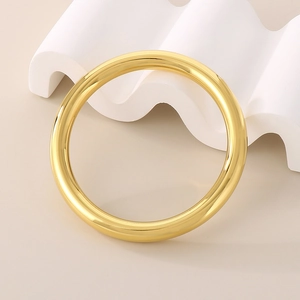 Polished gold hollow tube bangle made of premium stainless steel on a white pedestal