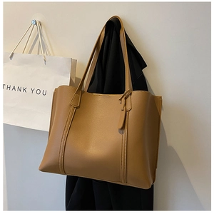 Detailed view of large brown soft leather tote bag hanging on a minimalist white wall