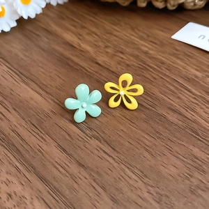 Detail of minimalist five-petal flower stud earrings in green and yellow on a wood surface