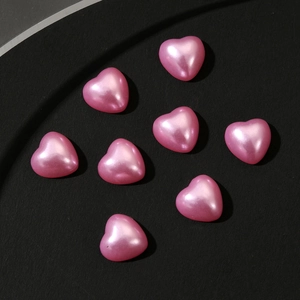 Detailed view of eight pink pearlescent 3D heart beads on a black textured surface
