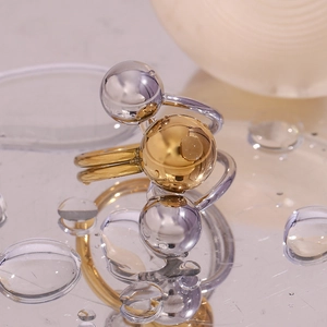 Close-up of a two-tone adjustable ring with gold and silver spheres on a water droplet surface