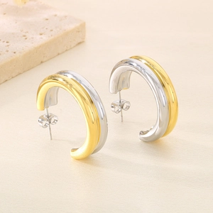 Détail des boucles d'oreilles bicolores en C sur pierre avec fond beige épuré