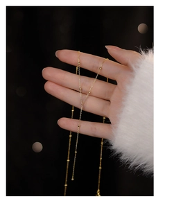 Close-up of minimalist gold beaded fringe necklace held by hand against a soft background