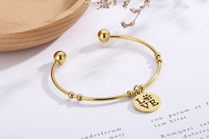 Detail shot of golden open bangle with LOVE heart charm and paw print engraving