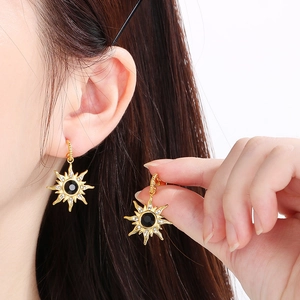 Détail de boucles d'oreilles étoile dorées avec gemmes noires et cristaux sur modèle