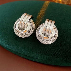 Close-up of silver hollow round earrings with twist rope design on green velvet pad