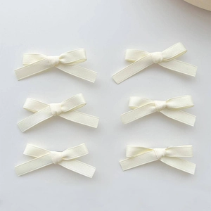 Top view of six white ribbon bow hair clips arranged neatly on a plain grey background