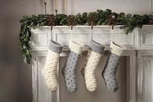 Detail of four knit Christmas stockings with fish scale pattern hanging on a white fireplace