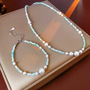 Elegant jewelry set with white pearls and light blue beads on a golden silk box