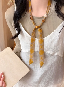 Detail view of a yellow printed chiffon necklace with wood and acrylic beads on a model