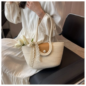 Close-up of a woven straw tote bag featuring a pearl button flap and delicate lace bow